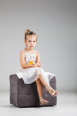 Mutlu küçük kız stüdyoda bir taburede oturup cips yiyor.