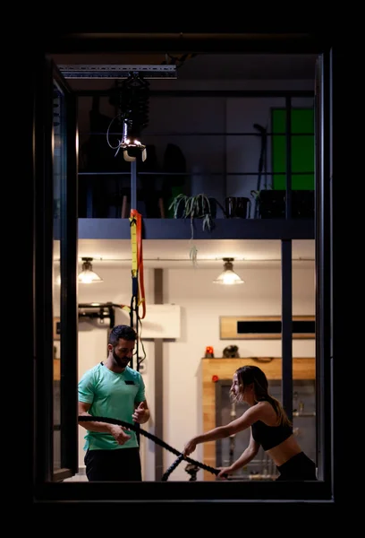 在健身室用绳子和男健身教练一起锻炼的女孩 从窗外看 — 图库照片