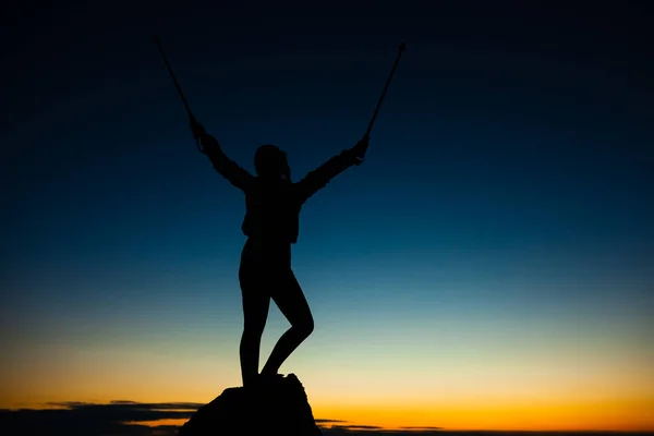 手を上げて岩の台座の上にハイカーの女の子のシルエット 青空の美しいオレンジ色の夕日 — ストック写真