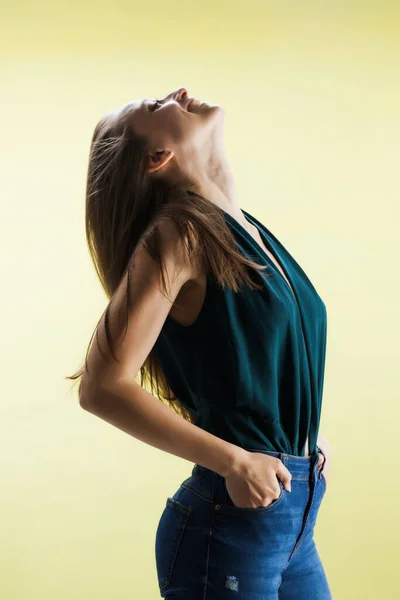 黄色の背景を持つ美しい女の子 ブルネット女性ともにファンシーシャツとジーンズポーズでスタジオ — ストック写真