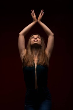 Koyu kırmızı arka plana karşı sevimli bir kız. Süslü tişörtlü, elleri havada esmer kadın yukarı bakıyor.