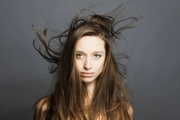 brunette girl with flowing hair in the air studio portrait against gray background.