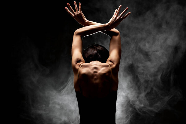 Half silhouette modern ballet dancer posing on dark background with smoke