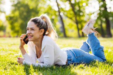 Parktaki bir tarlada yatan güzel kız. Telefonda konuşuyorlar..