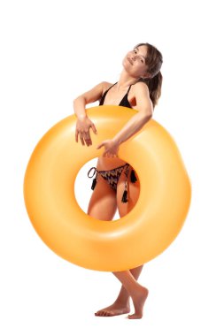 Siyah mayo giymiş, elinde turuncu şişirilebilir lastik yüzük tutan güzel, genç ve seksi bir kadın beyaz arka planda izole edilmiş. Yaz havuzu tatil köyü konsepti.
