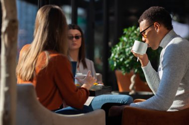 Three friends in a restaurant talking smiling and drinking tea. Business colleagues having a meeting after work or during coffee break at a cafe bar.