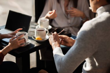 Three friends in a restaurant talking and having tea. Business colleagues in a meeting after work or during coffee break at a cafe bar. Abstract photo focus on tea cup