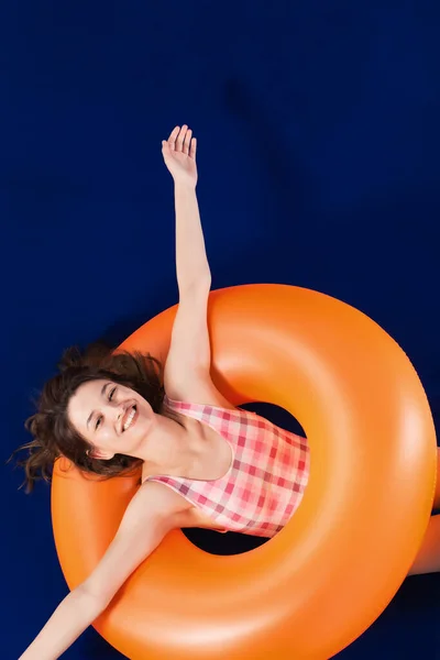 快乐的女孩穿着一件粉红色的泳衣 躺在充气橙色的橡胶圈上 暑假的概念 蓝色表面和背景 — 图库照片