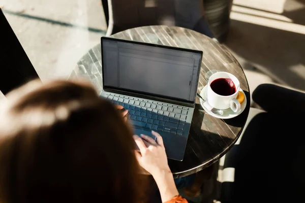 明るい日差しのカフェバーやレストランで若い実業家 フリーランサーの女の子はノートパソコンで働いていて 窓のテーブルでお茶を飲んでいます 要旨写真 — ストック写真