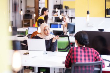 Modern bir ofis alanında masaüstü ve dizüstü bilgisayarlar üzerinde çalışan yaratıcı gençler takımı.