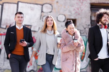 Bir grup insan sokakta güven içinde yürüyor. İş adamları ve iş kadınları birlikte seyahat ediyorlar. Arka planda tanımlanamayan eski duvar yazıları var..