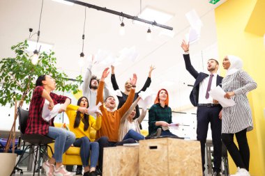 Modern ofis işyerindeki çok ırklı başarılı iş arkadaşlarının oluşturduğu takım başarıyı kutlamak için kağıt fırlatıyor. Çeşitlilik mutluluk kavramı.