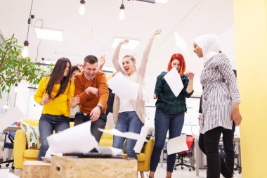 Modern ofis işyerindeki çok ırklı başarılı iş arkadaşlarının oluşturduğu takım başarıyı kutlamak için kağıt fırlatıyor. Çeşitlilik mutluluk kavramı.