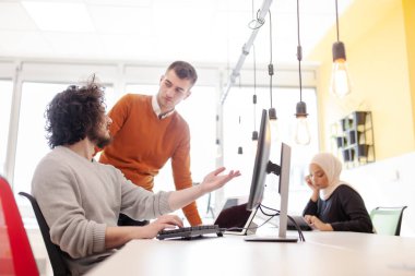 İş adamları bilgisayarın önünde sohbet ediyorlar. Modern çok ırklı ofis alanı. 