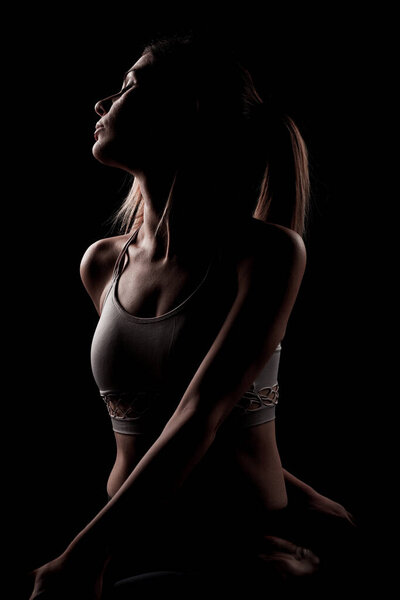 Красивая кавказская девушка позирует йогой в тени. фото с подсветкой сбоку на чёрном фоне.