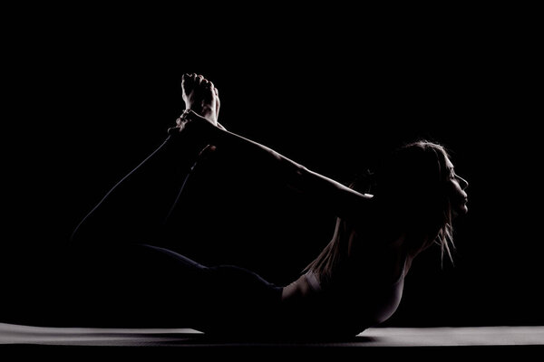 Beautiful caucasian girl posing yoga in shadow. side lit photo on black background.