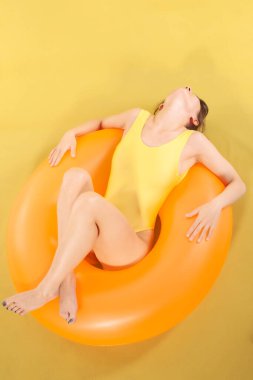 Şişme lastik halkanın üzerinde tek parça sarı mayo giymiş bir kız yatıyor. Yaz tatili kavramı.