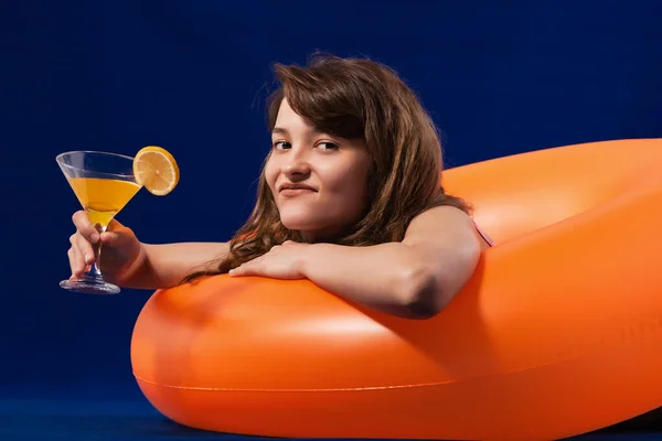 アルコールカクテルを保持インフレータブルオレンジゴムリング上のワンピース水着の女の子 夏休みのコンセプト 青の背景 — ストック写真