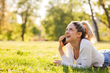 Parktaki bir tarlada yatan güzel kız. Telefonda konuşuyorlar..