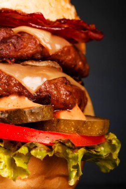 Abstract double burger with bacon cheese onions tomatoes cucumber and lettuce. Against dark background.