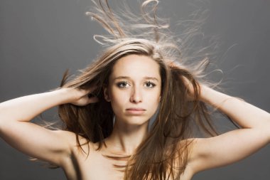 Havada dalgalı saçları olan esmer kız. Stüdyoda gri arka planda portresi olan..