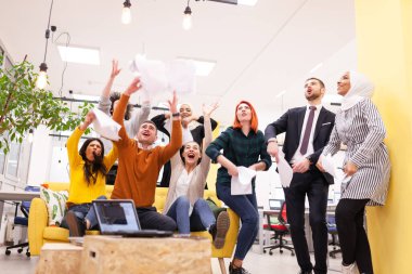 Modern ofis işyerindeki çok ırklı başarılı iş arkadaşlarının oluşturduğu takım başarıyı kutlamak için kağıt fırlatıyor. Çeşitlilik mutluluk kavramı.