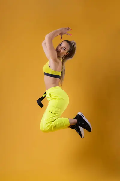 stock image Beautiful happy girl in yellow outfit jumping against dark yellow or orange background.