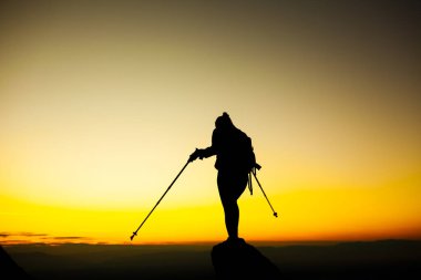 Kaya kaidesinde elleri havada gezen bir kızın silueti. Güzel turuncu gün batımı.