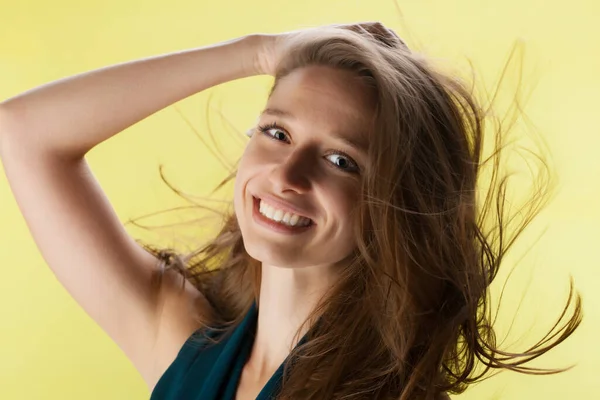 Beautiful girl with flowing hair against yellow background. Brunette lady with fancy shirt and jeans posing in studio.