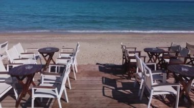 Kafe ya da restoran sandalyeleri ve deniz kenarındaki ahşap bir platformda masalar. Gökyüzü boş sahil manzarası.