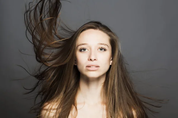 brunette girl with flowing hair in the air studio portrait against gray background.