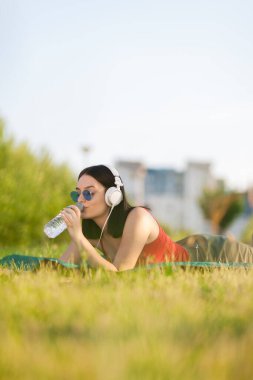 Parkta plastik bir su şişesiyle yatan güzel bir kız. Güneşli bir yaz gününün tadını çıkarıyorum..