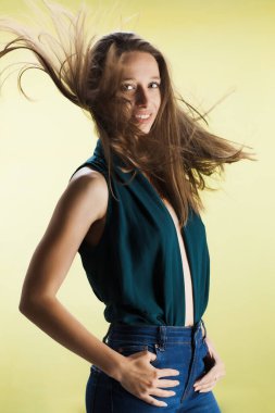Sarı arka planda dalgalı saçları olan güzel bir kız. Süslü gömlekli ve kot pantolonlu esmer kadın stüdyoda poz veriyor..