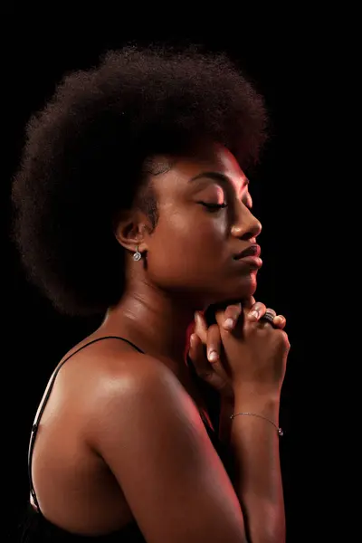 Studio portrait of elegant african american lady with curly hair afro hairstyle against black background. Girl in black dress.