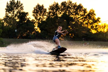 Dişi wakeboardcu gün batımında uyanıyor. Su kayağı yapan bir kız. Çekici ipi tutuyorum. Gölde yaz aktiviteleri.
