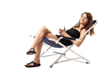 Plaj sandalyesinde oturan genç ve güzel bir kız elinde beyaz arka planda izole edilmiş boş bira bardağı tutuyor. Yaz konsepti.