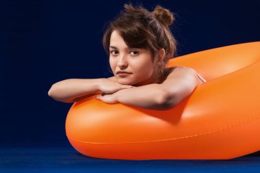 Şişirilebilir turuncu lastik halkada yüzen ciddi bir kız. Yaz tatili kavramı. Mavi yüzey ve arkaplan.