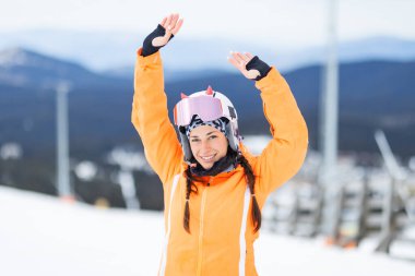 Kayakçı kız poz veriyor ve karda el hareketi yapıyor..
