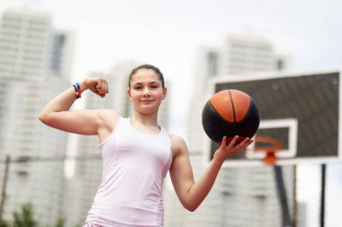 Basketbolcu portresi. Poz veren ve kaslarını gösteren kız. Kentsel geçmişe sahip açık hava sporları sahası.