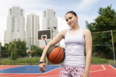 Basketbol oynayan güzel bir genç kızın portresi. Topu elinde tutuyor. Kentsel çevrede açık hava spor sahası.