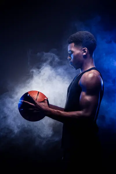 青い霧の背景に対してボールを保持するバスケットボール選手 バスケットを見ている筋肉アフリカ系アメリカ人男性 — ストック写真
