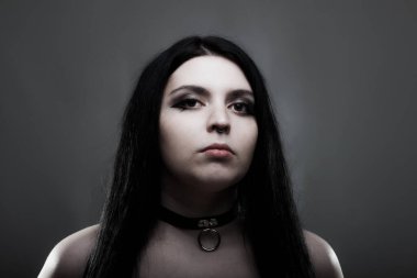 Koyu gri arka planda beyaz gözlü, uzun siyah saçlı gotik kız..