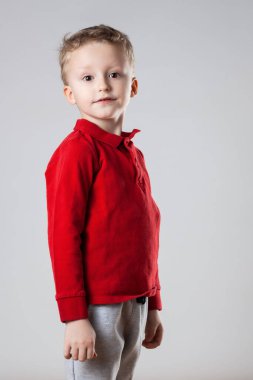 Kırmızı bluzlu, dik duran ve kameraya bakan mutlu bir çocuğun portresi..