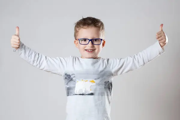 一个戴眼镜的小男孩热切地举起一个大拇指 免版税图库图片