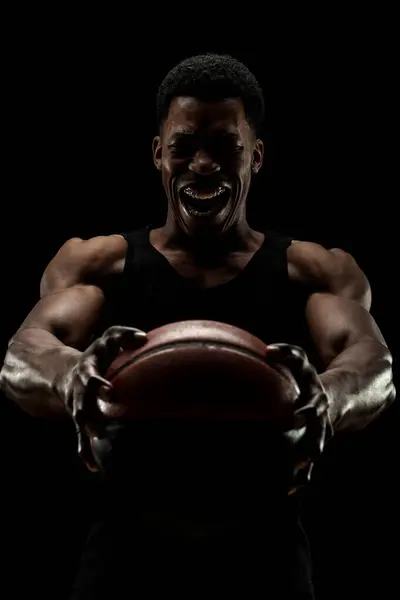 篮球运动员拿着一个黑色背景的球 尖叫的非洲裔美国人轮廓 图库照片