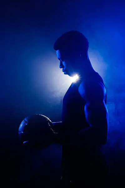 篮球运动员在蓝雾的背景下持球 肌肉发达的非洲裔美国人的轮廓 图库图片