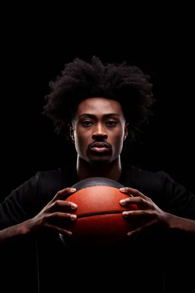 篮球运动员拿着一个黑色背景的球 严重集中的非洲裔美国人 图库图片