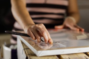 Resim aletleriyle çevrili bir tuval üzerinde ustalıkla çalışan bir kadın sanatçının ellerine yakından bakın..