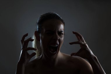 Dramatic image capturing the intense emotion of a woman screaming with her hands claw-like in the air. The lighting accentuates the tension and raw energy portrayed. clipart