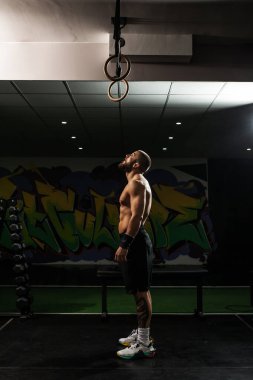 Kararlı bir erkek sporcu jimnastik yüzüklerine bakar, spor salonunda spor yapmadan önce odaklanır..